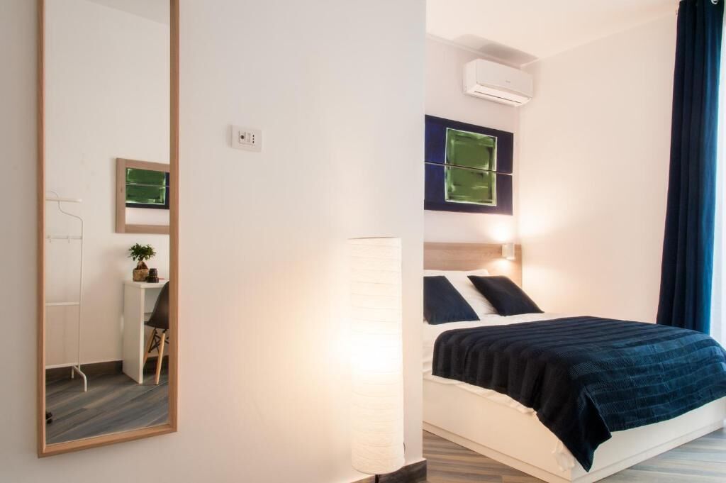 Une chambre d’hôtel équipée d’un lit, d’un bureau, d’une chaise, d’un miroir et d’un climatiseur fixé au mur.