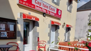 A building with a sign for 'Captain Cook' and a 'PUB' sign. There are outdoor tables and red chairs.