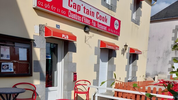 Een terras met rode stoelen en tafels, een bord met 'Captain Cook', een pub en restaurant, en een kleine tuin met een houten omheining.