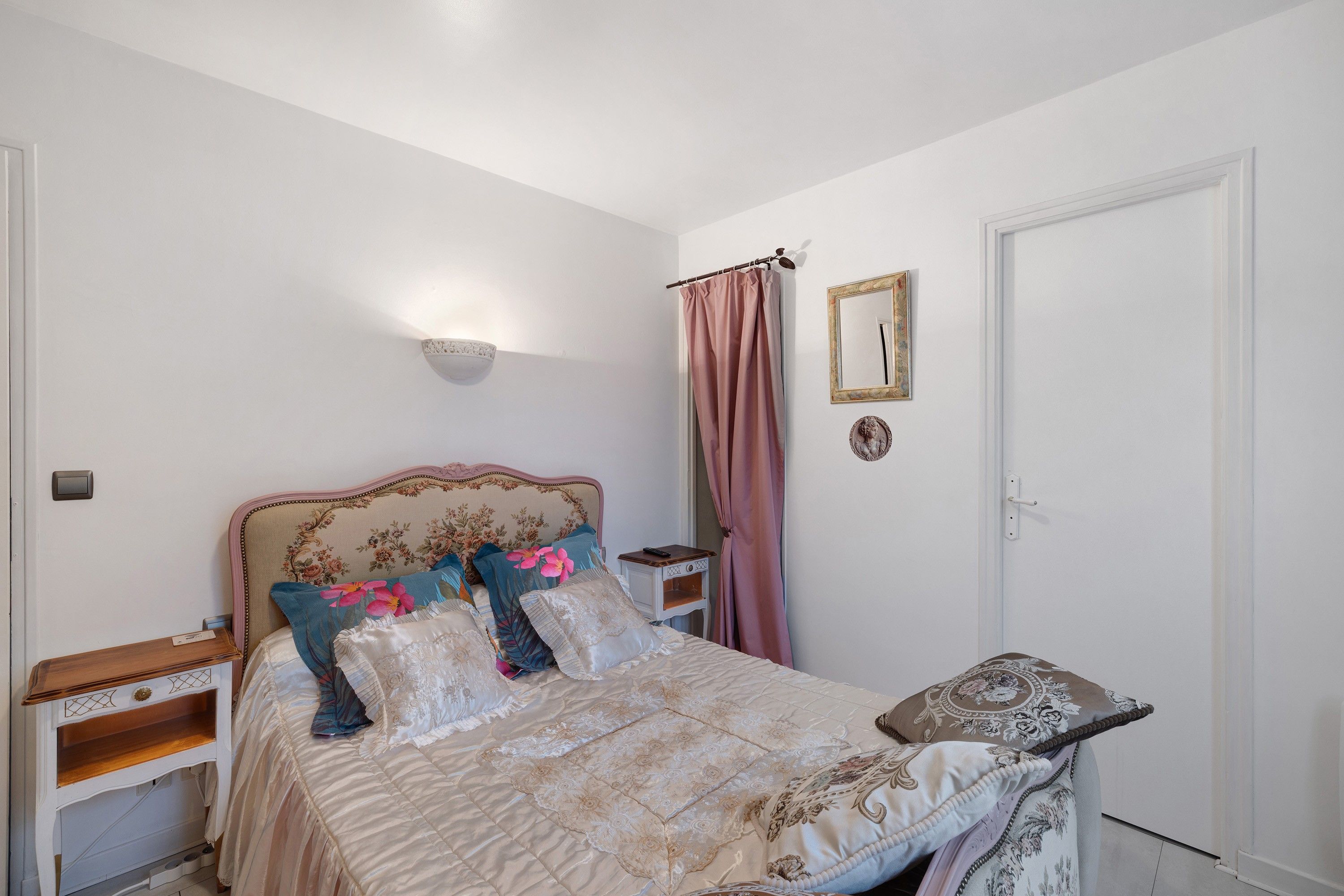 Een slaapkamer met een bed, nachtkastjes, een lampje aan de muur, een deur en een spiegel.