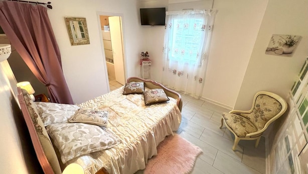A bedroom with a bed, a chair, a television, and a window with curtains.