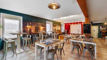Un restaurante con varias mesas y sillas, un escenario con cortina roja y un menú en una pizarra.