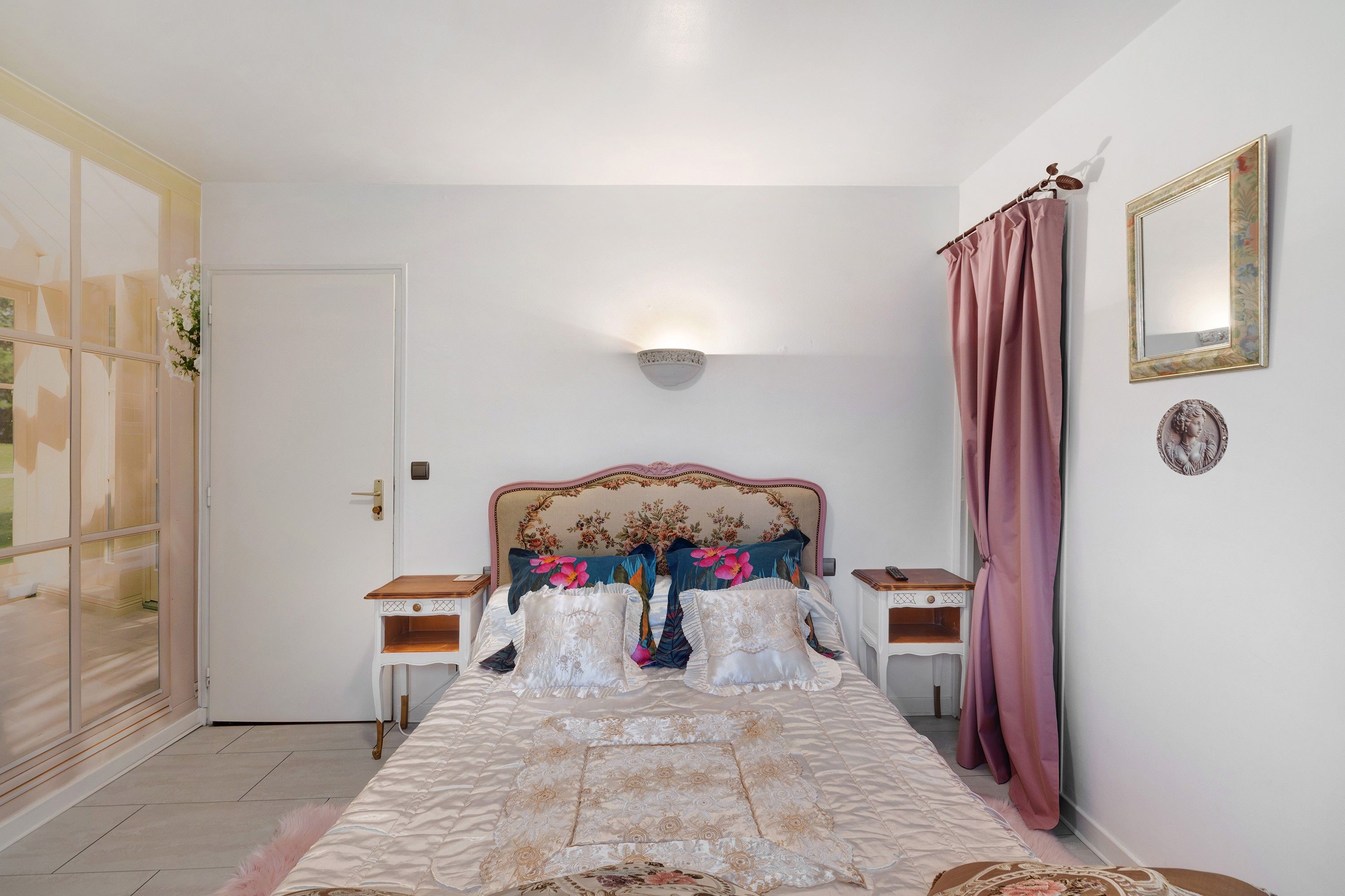 Un dormitorio con cama, mesitas de noche, un espejo y una puerta.