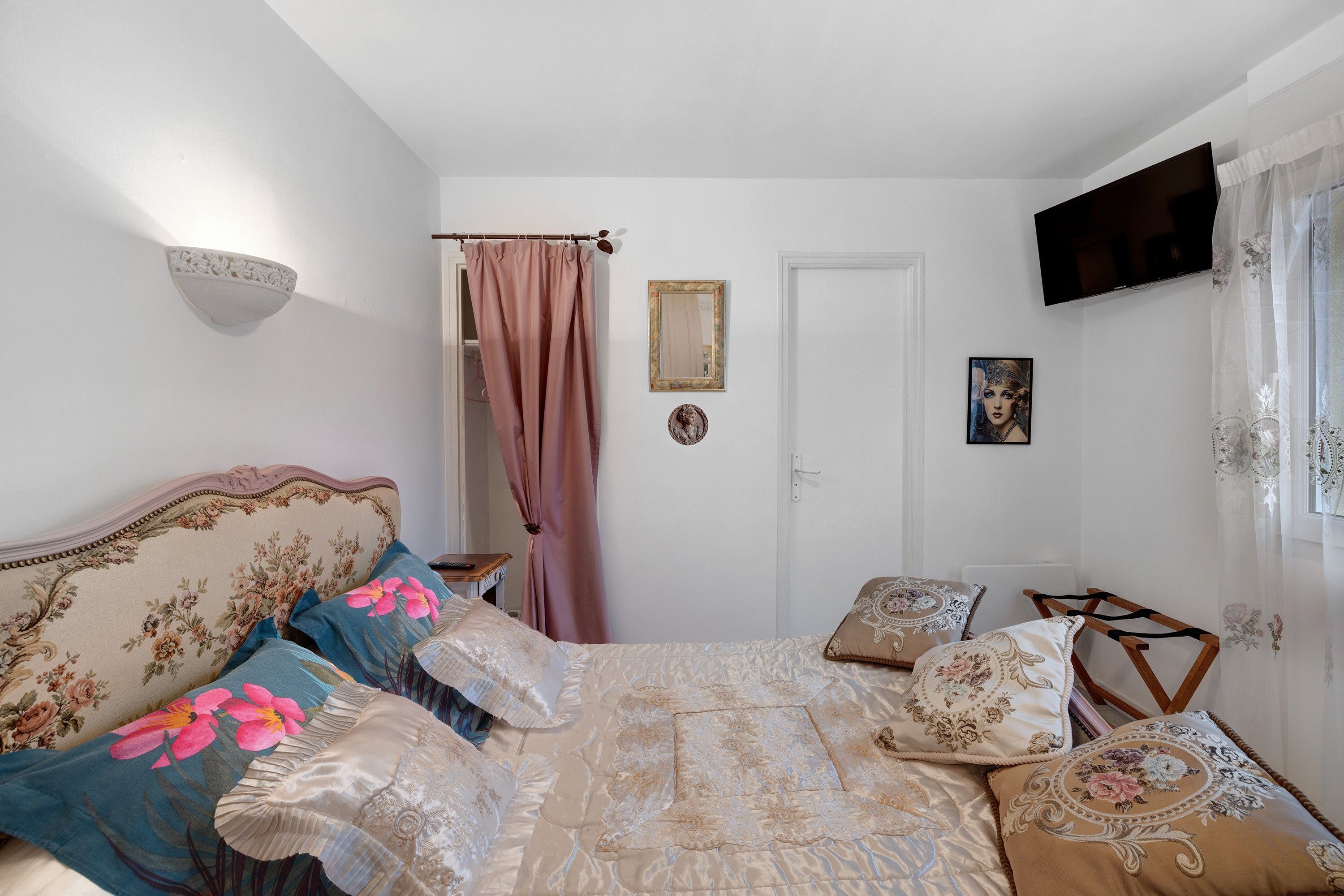 A bedroom with a bed, a bedside table, a TV mounted on the wall, and a door.