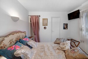 A bedroom with a bed, a bedside table, a TV mounted on the wall, and a door. - Bed and Breakfast 'Chambre Romantique' with Wi-Fi (Caurel)