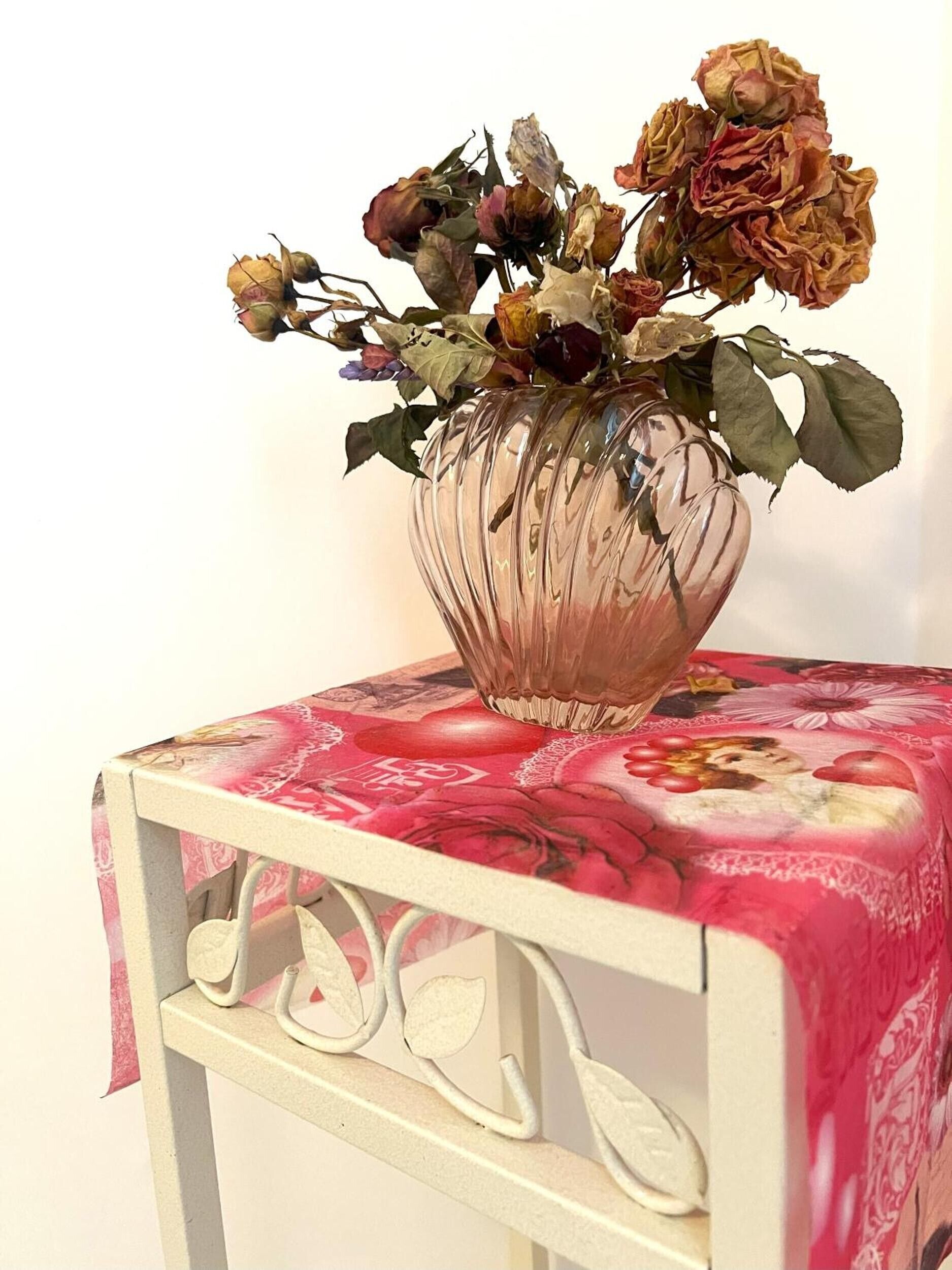Un jarrón con flores secas sobre una mesa con mantel floral.