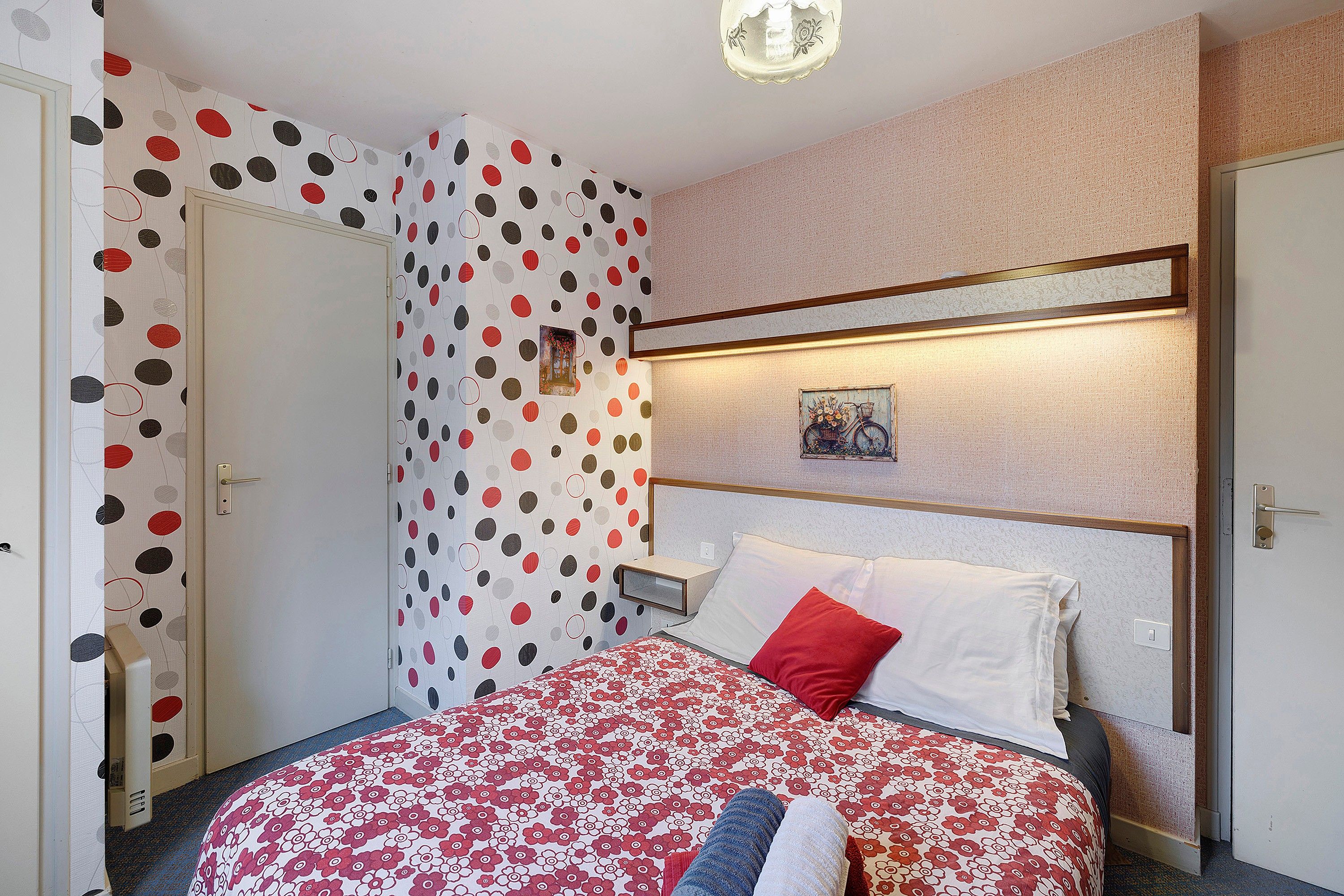 A hotel room with a bed, a nightstand, a wall-mounted picture, and a door.