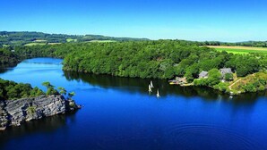 Un río rodeado de abundante vegetación y algunos edificios, con barcos en el agua.