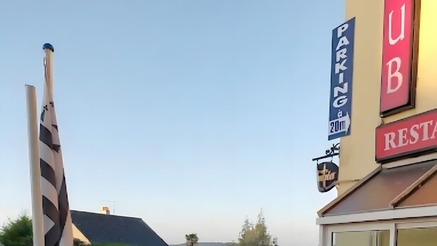 Un área de estar al aire libre con sillas rojas y una mesa, con un cartel que dice 'PARKING' y 'RESTAURANT', y una vista de la calle y edificios al fondo.