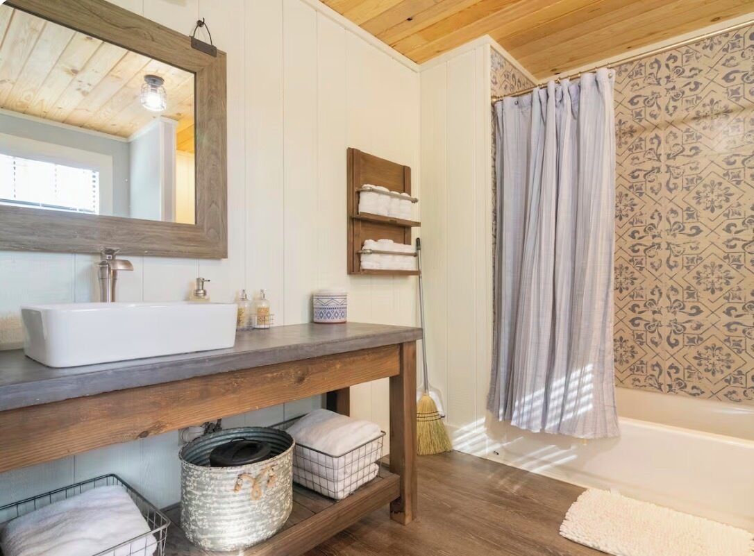Un baño con tocador de madera, un espejo grande, un lavamanos y cortina de ducha con diseño estampado.
