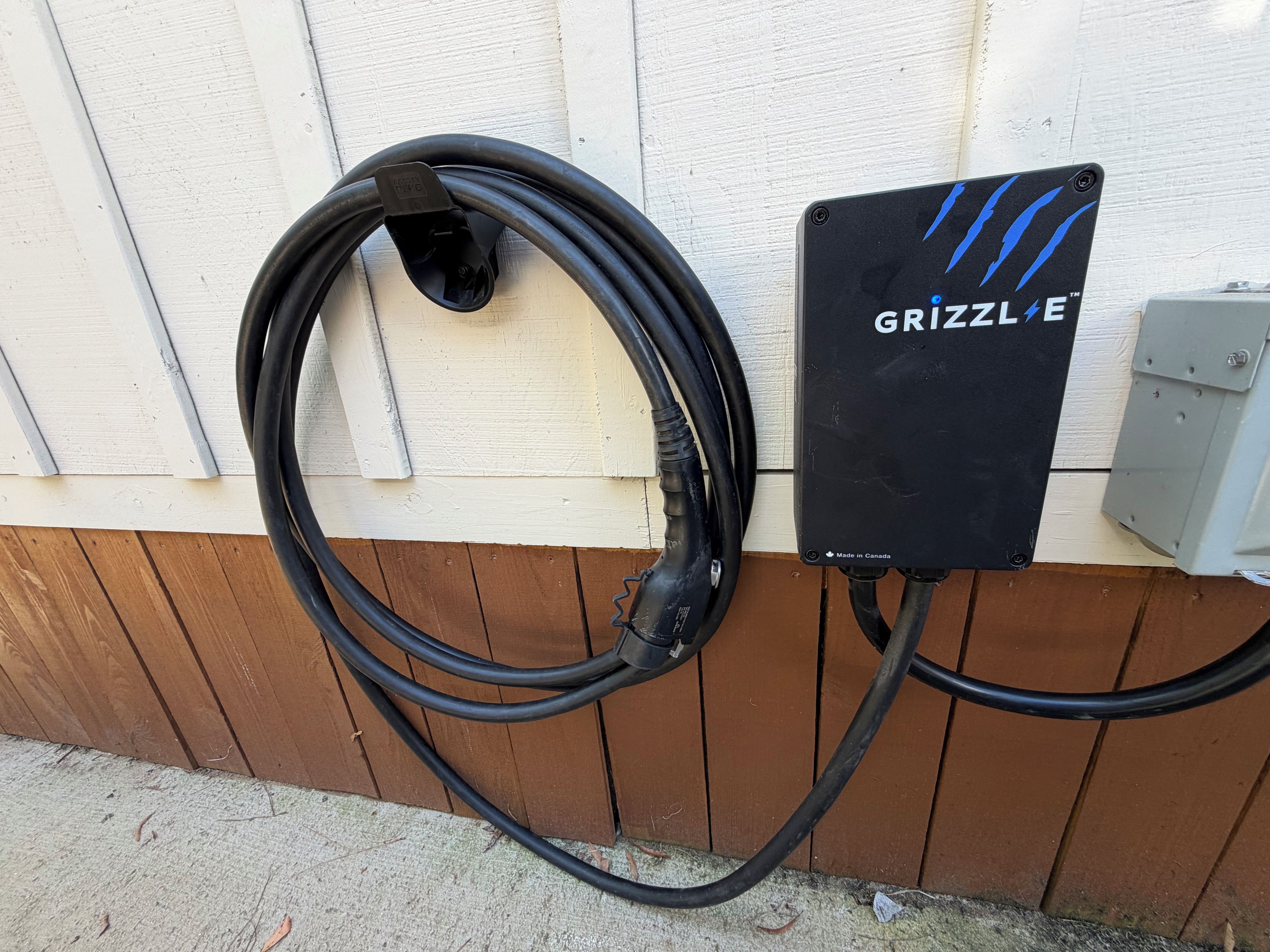 A black outdoor electrical box with a label 'GRIZZLE' and a coiled black cable connected to it.