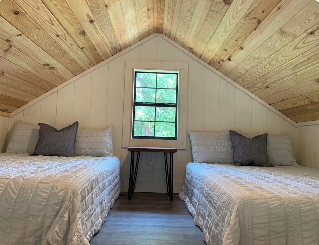 Un dormitorio con dos camas, una ventana y vigas de madera en el techo.