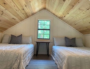 A bedroom with two beds, a window, and wooden ceiling beams.
