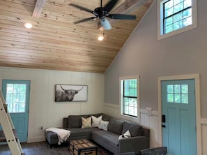 A room with a wooden ceiling, a gray sofa, a framed picture, and a door.