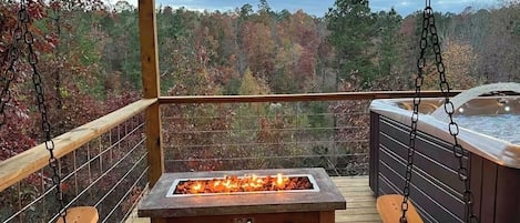 A wooden deck with a stone fire feature and a hot tub.