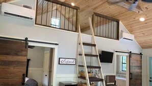 Een loft-achtige kamer met houten plafond, een hoogslaper, een ladder, een flatscreen-tv en een keuken met fornuis en spoelbak.