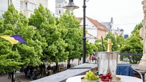 A table with a bottle of champagne, a tray of grapes, and a glass of water on an outdoor balcony with a city view. - The Royal Hlavna - Balcony Apartment (Old Town, Košice)