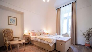 A bedroom with a bed, bedside table, chair, and a window with curtains. - The Royal Hlavna - Balcony Apartment (Old Town, Košice)