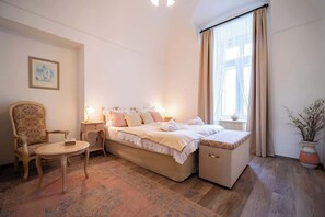 A bedroom with a bed, bedside table, chair, and a window with curtains.