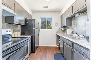A kitchen with dark cabinets, a black refrigerator, a window with a view, and a blue rug on the floor.