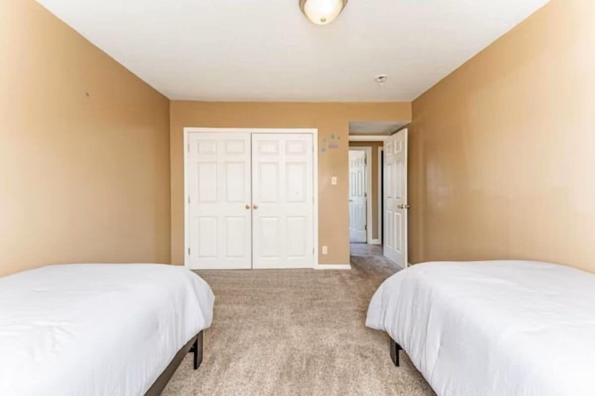 Una habitación con dos camas, paredes color beige y piso alfombrado.