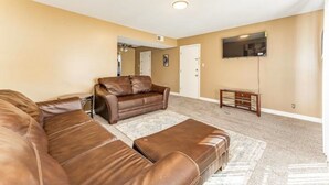Ein Wohnzimmer mit braunem Ledersofa, einem flachbildfernseher an der Wand und einem Holztisch.