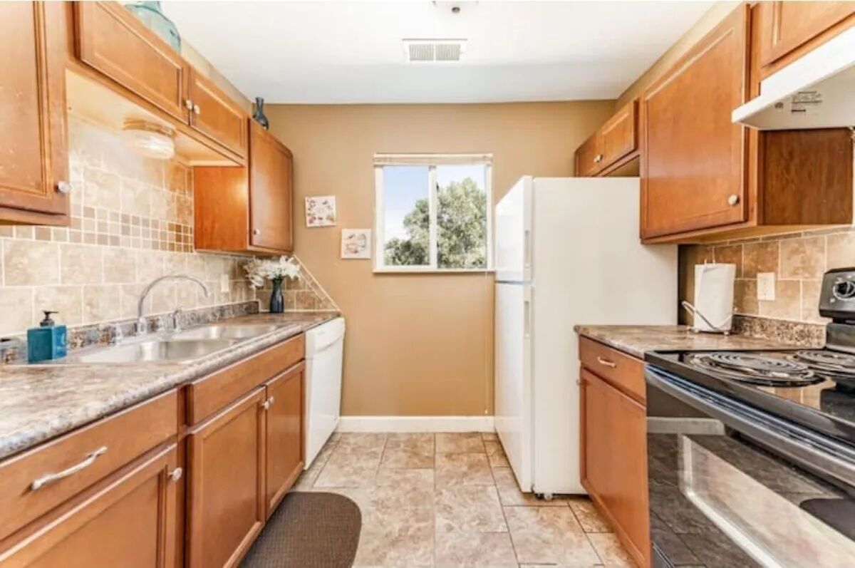 Una cocina con armarios de madera, un refrigerador blanco, una estufa y una ventana.