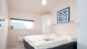 A bedroom with a bed, a window, a radiator, and a framed picture on the wall. - Helles Kustenhaus mit Sauna (Grossenbrode)