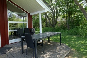 Eine Terrasse im Freien mit Tisch und Stühlen, einem überdachten Bereich und Blick ins Grünes.