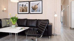A modern living room with a black leather sofa, a white coffee table, a potted plant, and two framed pictures on the wall. - Helles Kustenhaus mit Sauna (Grossenbrode)