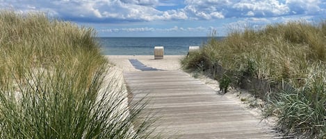 Una pasarela de madera que conduce a una playa con arena y césped a ambos lados.