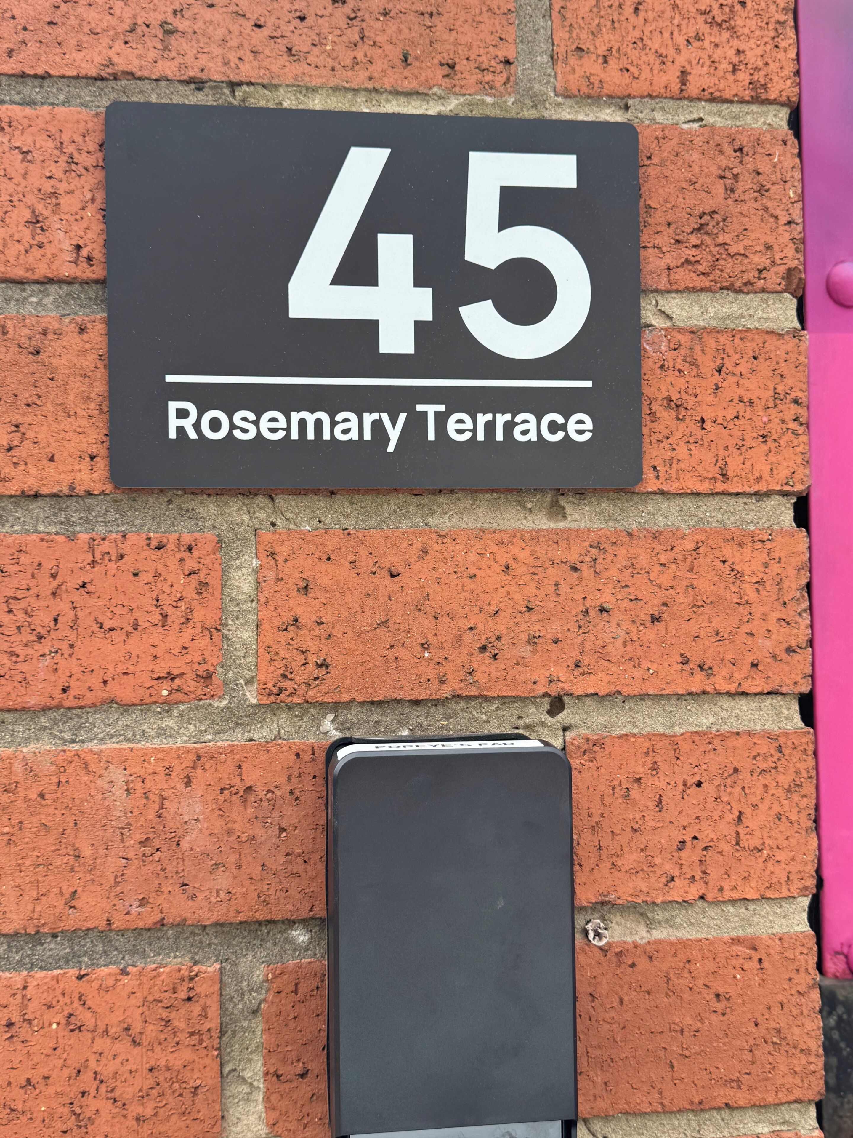 A black sign with white text indicating '45 Rosemary Terrace' mounted on a brick wall.