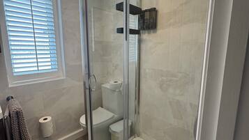 A modern bathroom with a glass-enclosed shower, a toilet, and a towel rack.