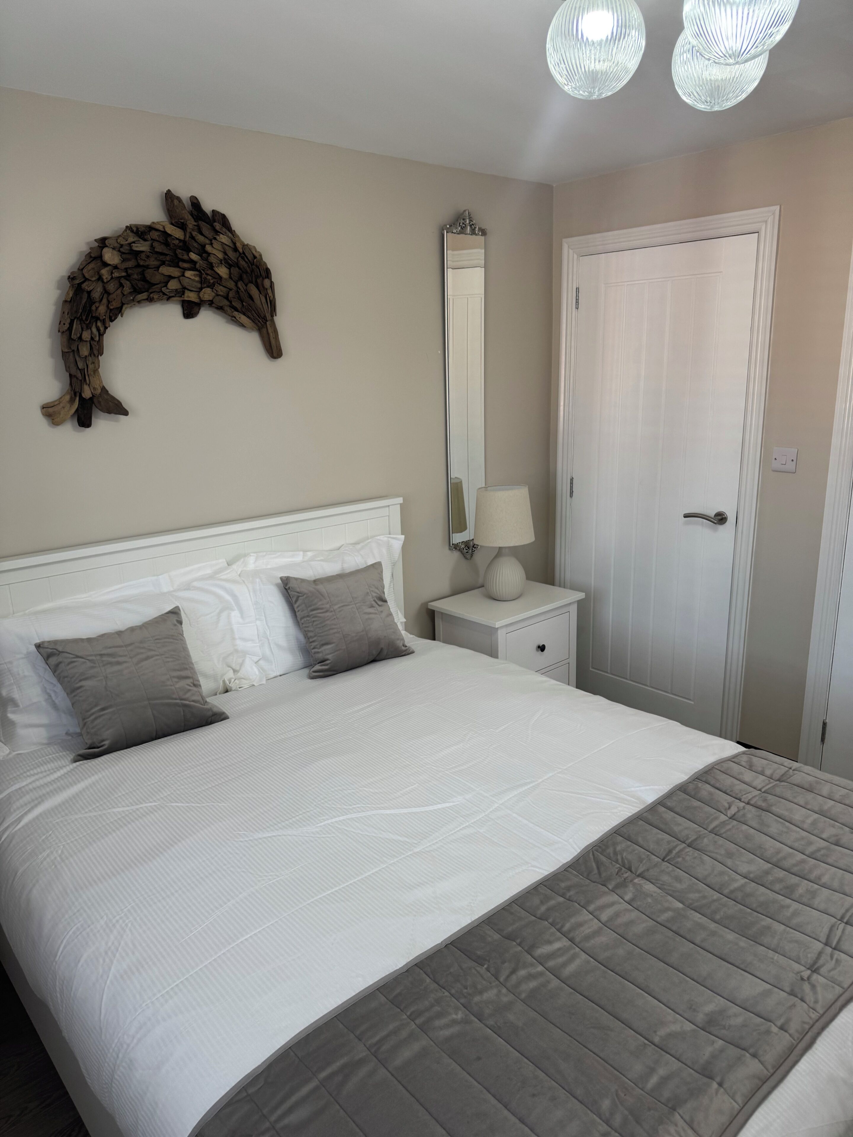 A neatly made bed with a white headboard, a bedside lamp, and a mirror on the wall.