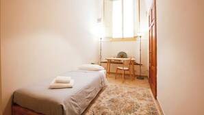 Ein kleines, gut beleuchtetes Schlafzimmer mit einem Bett, einem Schreibtisch und einem Stuhl.