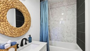 Un baño con un espejo redondo, un lavamanos blanco, una bañera y una cortina de ducha azul.