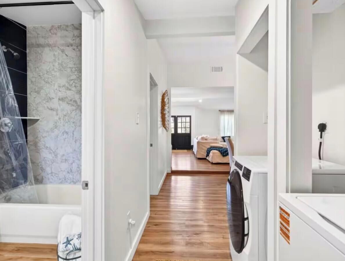 A modern interior with a hallway leading to a living area, a washing machine, and a bathroom with a shower.