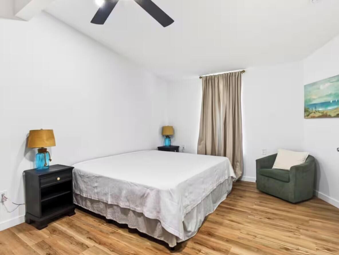 A bedroom with a bed, a nightstand, a lamp, a green chair, and a painting on the wall.