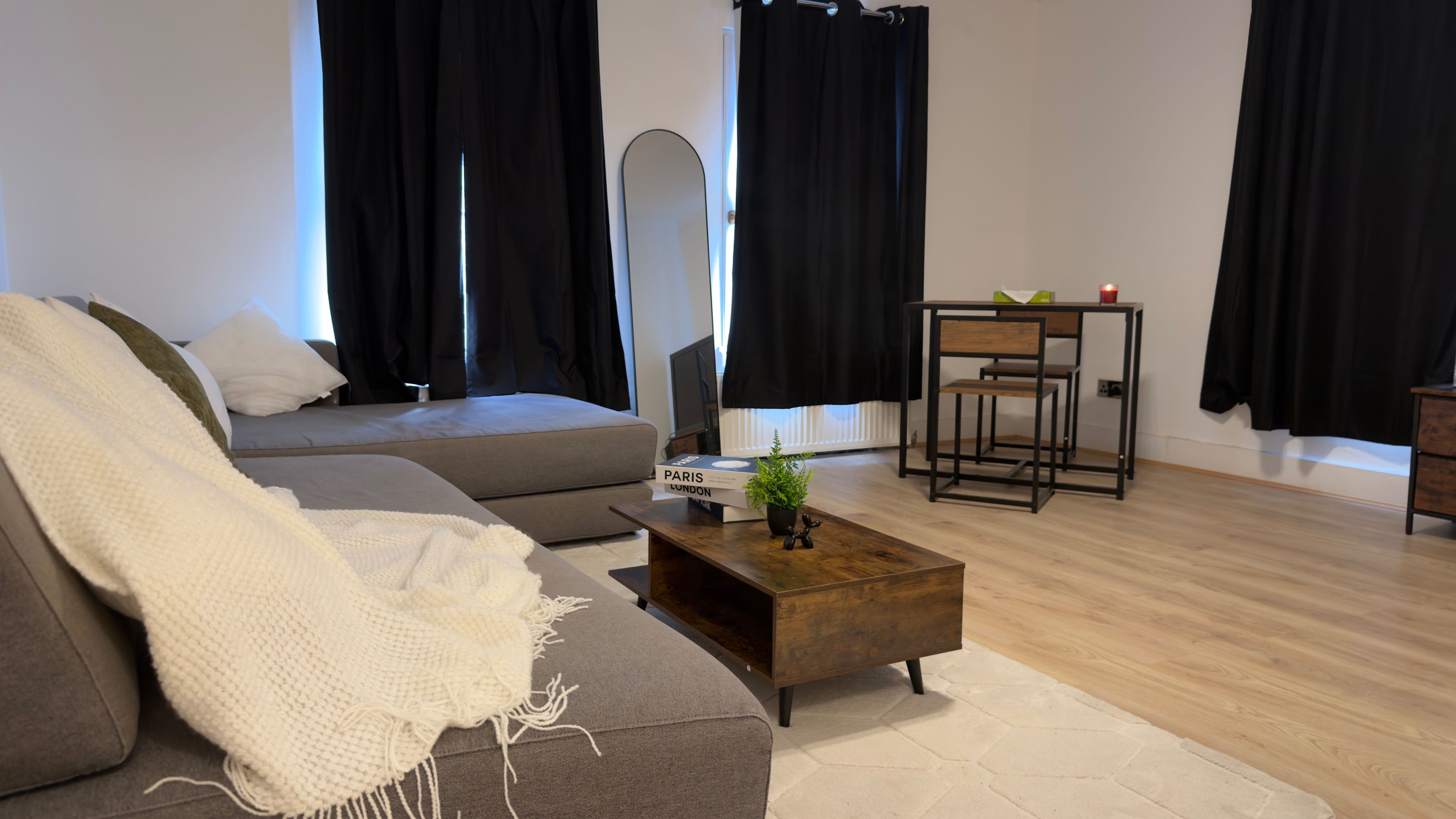 Un salon moderne avec un canapé gris, une table basse en bois et un fauteuil à monture noire.
