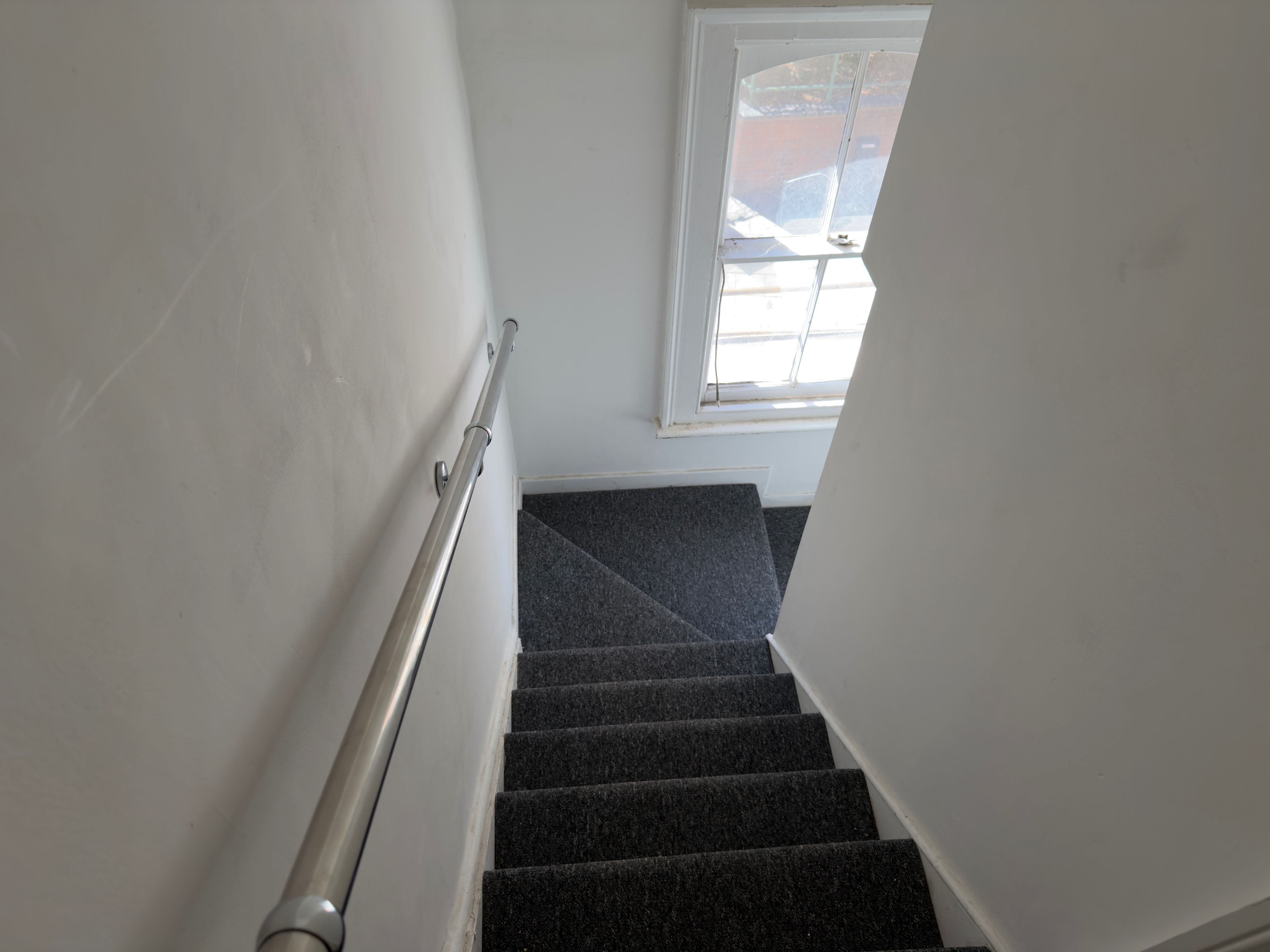 A staircase with a handrail, carpeted steps, and a window with a view of the outside.