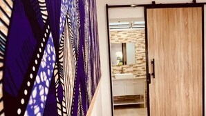 Una habitación con una mesa blanca, una puerta de madera y vistas a un baño con pared de piedra y un espejo.