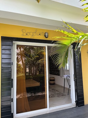 A yellow building with a sliding glass door entrance, a sign above the door, and a palm tree to the right.