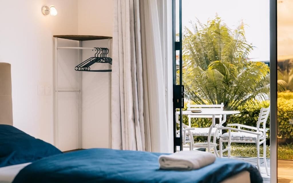 Un dormitorio con cama, perchero y vista a un espacio exterior con sillas y una mesa.