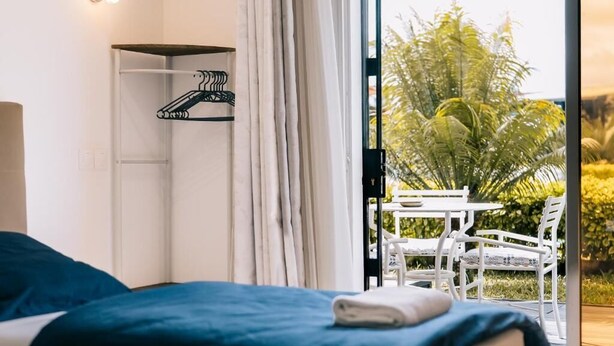 Un dormitorio con cama, perchero y vista a un espacio exterior con sillas y una mesa.