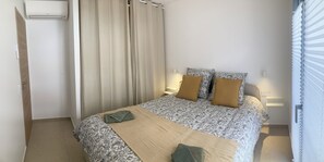 Une chambre à coucher avec un lit, des rideaux, une table de chevet et un climatiseur fixé au mur.