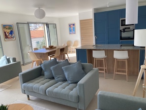 A modern living room with a grey sofa, a dining area with a wooden table and chairs, and a kitchen with blue cabinets and a built-in oven. - Villa central Cannes-4BR/3BA/8P-AC-free parking-12’ walk to Palais des Festival (Cannes)