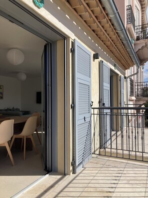 Ein Wohngebäude mit Schiebeglaseingang, einem Balkon mit Metallgeländer und einer gefliesten Terrassenfläche.