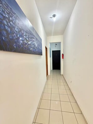 Ein Flur mit Fliesenboden, einem Gemälde an der Wand, einer Tür am Ende und einem Feuerlöscher an der Wand.