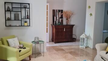 A living room with a green armchair, a white sofa, a coffee table, and a patterned rug.