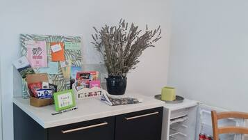 A kitchen area with a white countertop, black cabinets, a potted plant, and various items including a coffee maker, a box of tissues, and a small table with a chair.